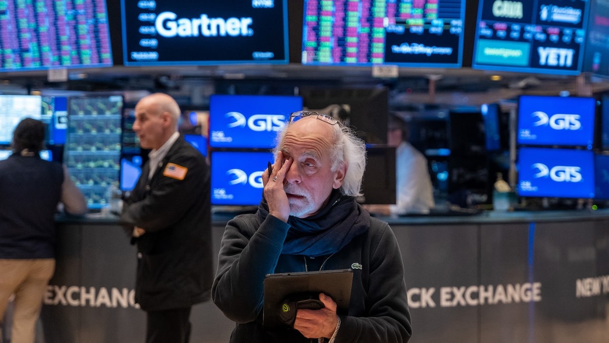 A visibly worried merchant has a tablet and rubs his eye on the New York Stock Exchange, with colored tickets and monitors who blink behind him.